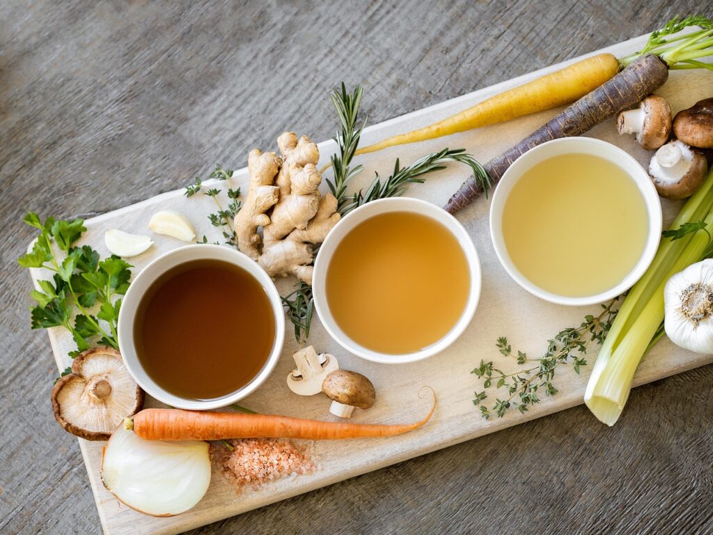 Bowls of bone broth with fresh vegetables on a wooden board